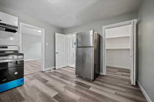 Kitchen with range hood, stainless steel appliances, light hardwood / wood-style flooring, and white cabinetry