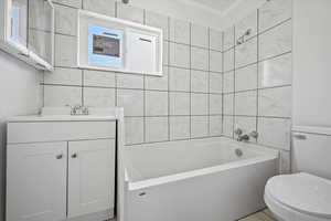 Full bathroom featuring tile walls, toilet, vanity, and  shower combination