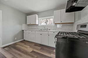 Kitchen featuring range hood, sink, white cabinetry, hardwood / wood-style flooring, and gas range