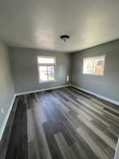 Empty room with dark hardwood / wood-style floors, a healthy amount of sunlight, and a textured ceiling