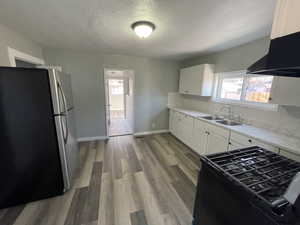 Kitchen with stainless steel fridge, light wood-type flooring, white cabinetry, and sink