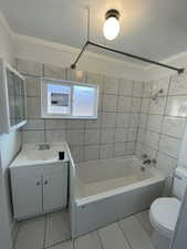 Full bathroom featuring tile patterned floors, toilet, vanity, tile walls, and tiled shower / bath