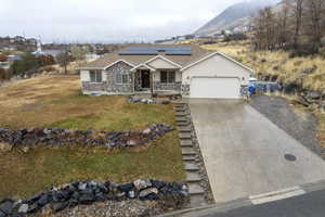 Ranch-style home with solar panels, a garage, a mountain view, a front lawn, and covered porch