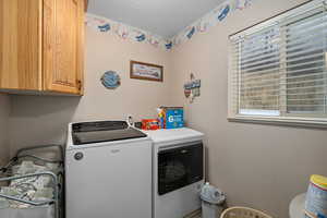 Laundry area featuring washer and clothes dryer, cabinets, and a textured ceiling