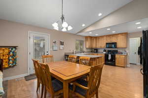 Dining room with a chandelier, light hardwood / wood-style floors, sink, and vaulted ceiling