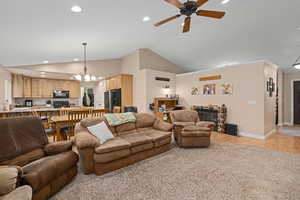 Living room featuring ceiling fan with notable chandelier, light hardwood / wood-style floors, sink, and high vaulted ceiling