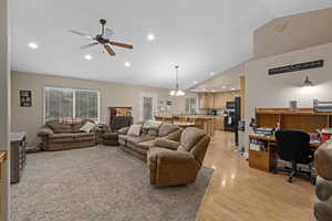 Living room with ceiling fan with notable chandelier, light hardwood / wood-style floors, and high vaulted ceiling