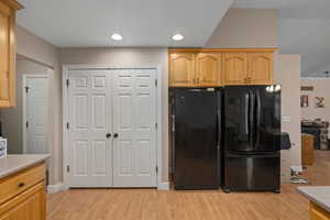 Kitchen featuring black refrigerator, light brown cabinetry, and light wood-type flooring