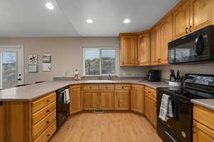 Kitchen with black appliances, light wood-type flooring, kitchen peninsula, and sink