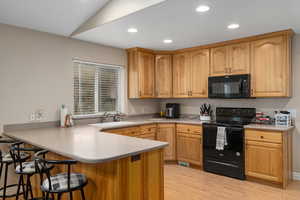 Kitchen with black appliances, a kitchen breakfast bar, sink, light wood-type flooring, and kitchen peninsula