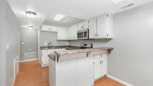 Kitchen with white cabinets, stainless steel appliances, kitchen peninsula, and light hardwood / wood-style flooring