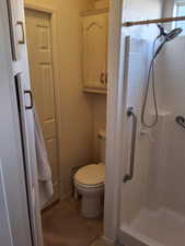 Bathroom with tile patterned floors, a tile shower, and toilet