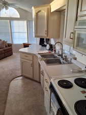 Kitchen with light colored carpet, ceiling fan, sink, white electric range, and lofted ceiling