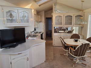 Kitchen featuring white cabinetry, sink, carpet floors, vaulted ceiling, and decorative light fixtures