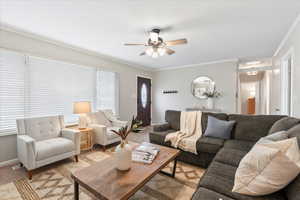 Living room with ceiling fan, light colored carpet, and ornamental molding