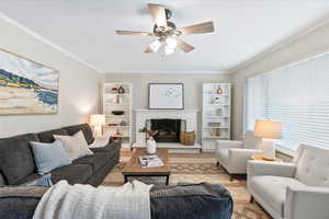 Living room with a stone fireplace, ceiling fan, and ornamental molding