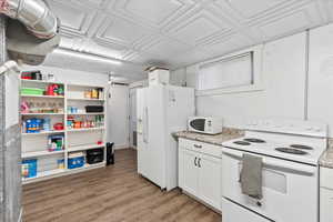 Kitchen with white appliances, hardwood / wood-style flooring, and white cabinetry