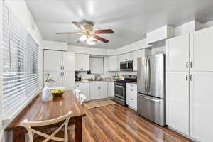 Kitchen featuring dark wood-type flooring, white cabinets, sink, ceiling fan, and stainless steel appliances