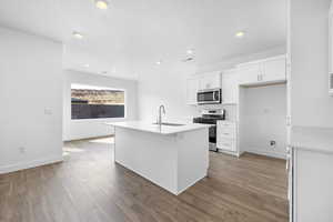 Kitchen featuring stainless steel appliances, dark wood-type flooring, sink, a center island with sink, and white cabinets