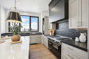 Kitchen with light wood-type flooring, custom exhaust hood, sink, pendant lighting, and double oven range