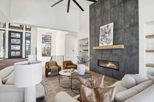 Living room with ceiling fan, built in features, hardwood / wood-style floors, a towering ceiling, and a tiled fireplace