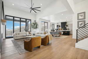 Living room with ceiling fan, a towering ceiling, and light wood-type flooring