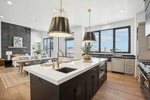 Kitchen with ceiling fan, sink, decorative light fixtures, a kitchen island with sink, and light wood-type flooring