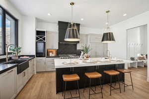 Kitchen with pendant lighting, wall chimney exhaust hood, and an island with sink