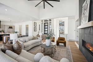 Living room featuring ceiling fan, sink, a high ceiling, wood-type flooring, and a tiled fireplace