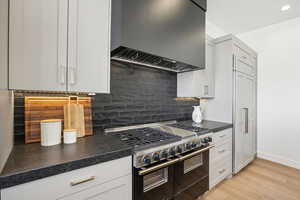 Kitchen featuring decorative backsplash, wall chimney exhaust hood, high end stainless steel range, white cabinets, and light hardwood / wood-style floors