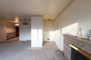 Unfurnished living room featuring crown molding, carpet, and a notable chandelier