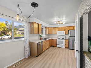 Kitchen with appliances with stainless steel finishes, sink, a notable chandelier, light hardwood / wood-style floors, and hanging light fixtures