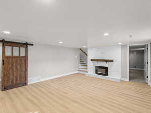 Unfurnished living room with a large fireplace, a barn door, and light wood-type flooring