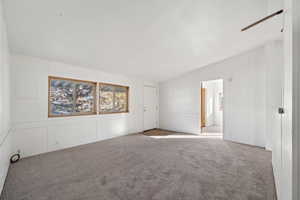 Carpeted empty room featuring vaulted ceiling and ceiling fan