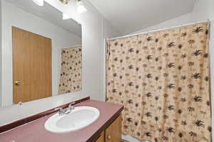 Bathroom with vanity, curtained shower, and vaulted ceiling