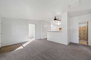 Unfurnished living room featuring dark colored carpet, ceiling fan, and lofted ceiling