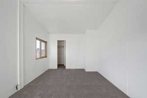 Empty room featuring vaulted ceiling and dark carpet