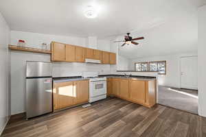 Kitchen with stainless steel fridge, kitchen peninsula, dark wood-type flooring, and white range with gas cooktop