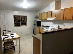 Kitchen featuring white gas stove, stainless steel fridge, a textured ceiling, and vaulted ceiling