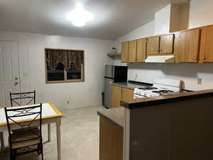 Kitchen featuring kitchen peninsula, stainless steel fridge, white gas range oven, a textured ceiling, and vaulted ceiling