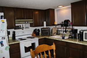 Duplex # B Kitchen with a textured ceiling, white appliances, dark brown cabinetry, and sink