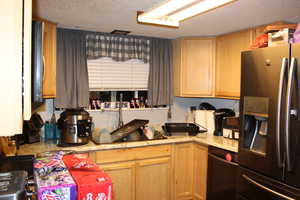 Duplex # A kitchen with a textured ceiling, dishwasher, light brown cabinets, and stainless steel refrigerator with ice dispenser