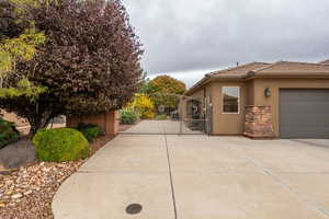 View of side of property featuring a gate, stucco siding, concrete driveway, a garage, and stone siding