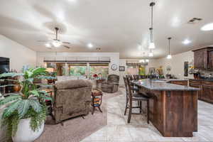 Kitchen featuring dark stone counters, dark brown cabinets, a breakfast bar area, a kitchen island with sink, and decorative light fixtures