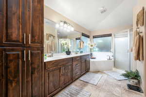 Bathroom with a bath, double vanity, a stall shower, light tile patterned floors, and vaulted ceiling