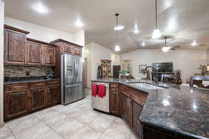 Kitchen with dark brown cabinetry, stainless steel appliances, lofted ceiling, decorative light fixtures, and dark stone counters