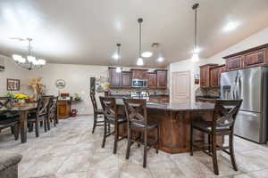 Kitchen featuring an island with sink, stainless steel appliances, decorative light fixtures, dark brown cabinets, and a breakfast bar