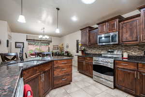 Kitchen with dark brown cabinetry, stainless steel appliances, dark stone countertops, hanging light fixtures, and light tile patterned floors