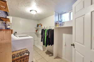 Clothes washing area with light tile patterned flooring, a textured ceiling, and washing machine and clothes dryer