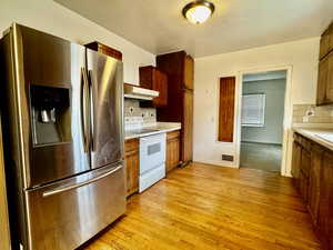 Kitchen with decorative backsplash, stainless steel fridge, white electric range oven, and light hardwood / wood-style floors